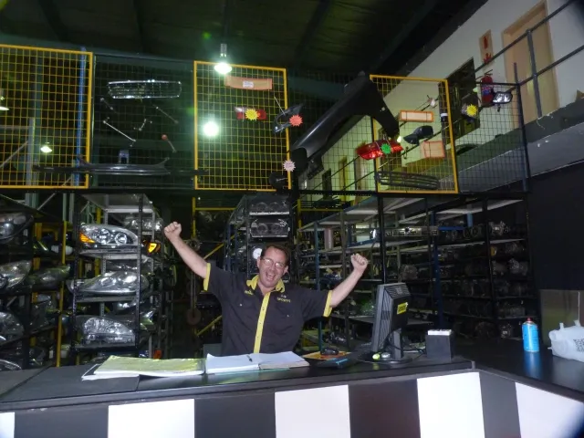 A SparesBoyz staff member at the warehouse counter, racking of stock behind him